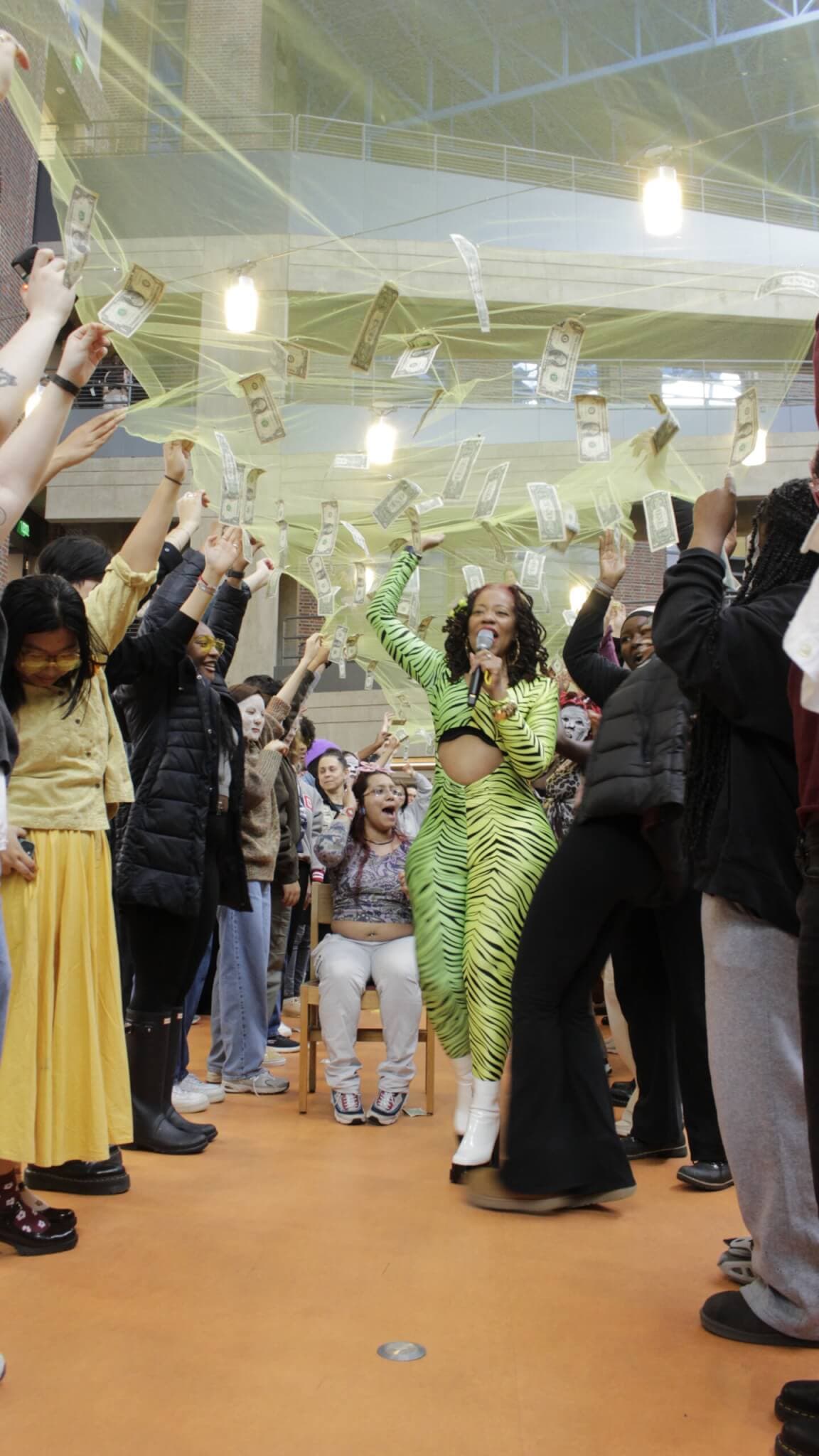 A woman in a green suit and a crowd celebrate as bills hang in the air overhead.