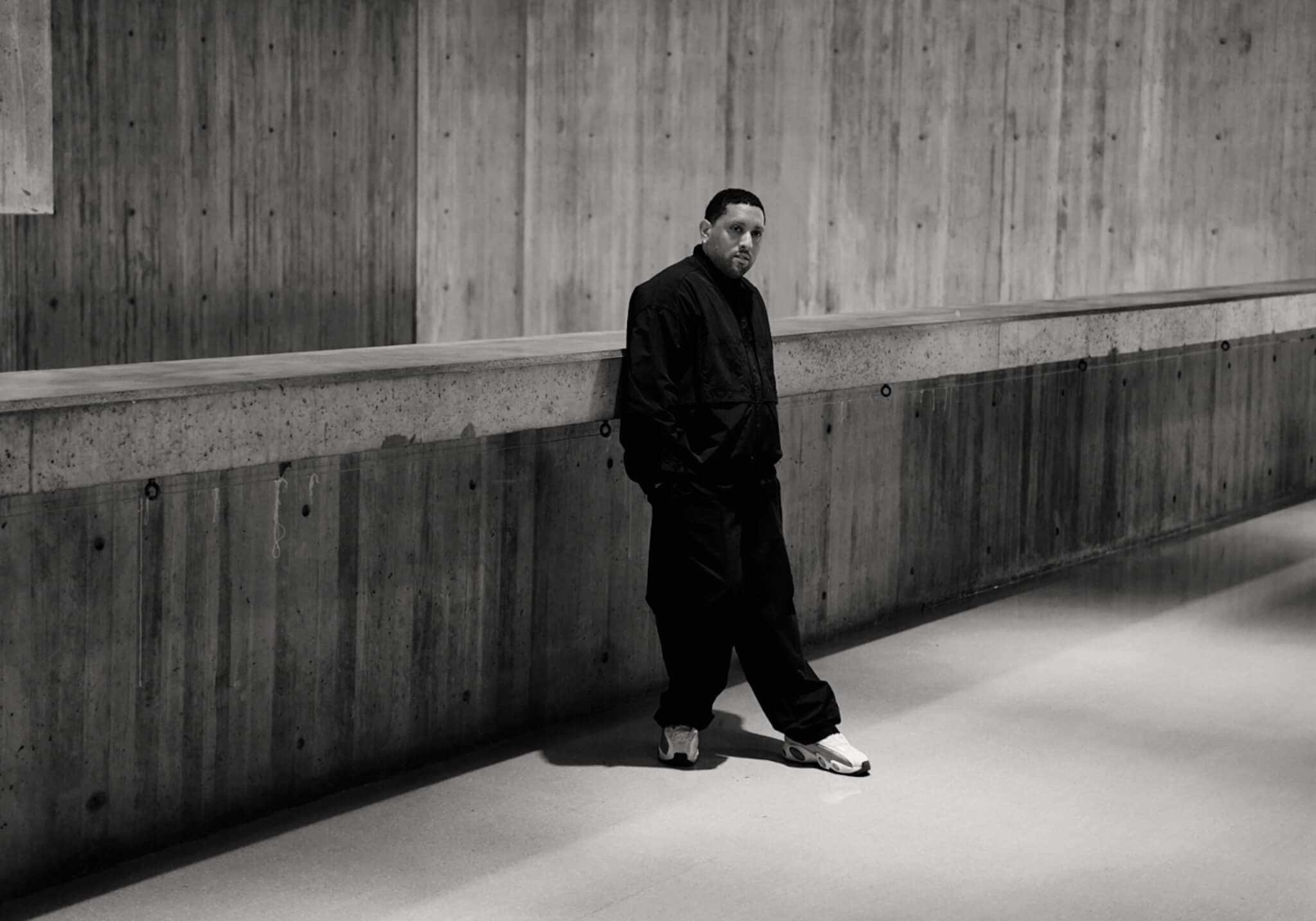 A man leans up against a wood-paneled wall.